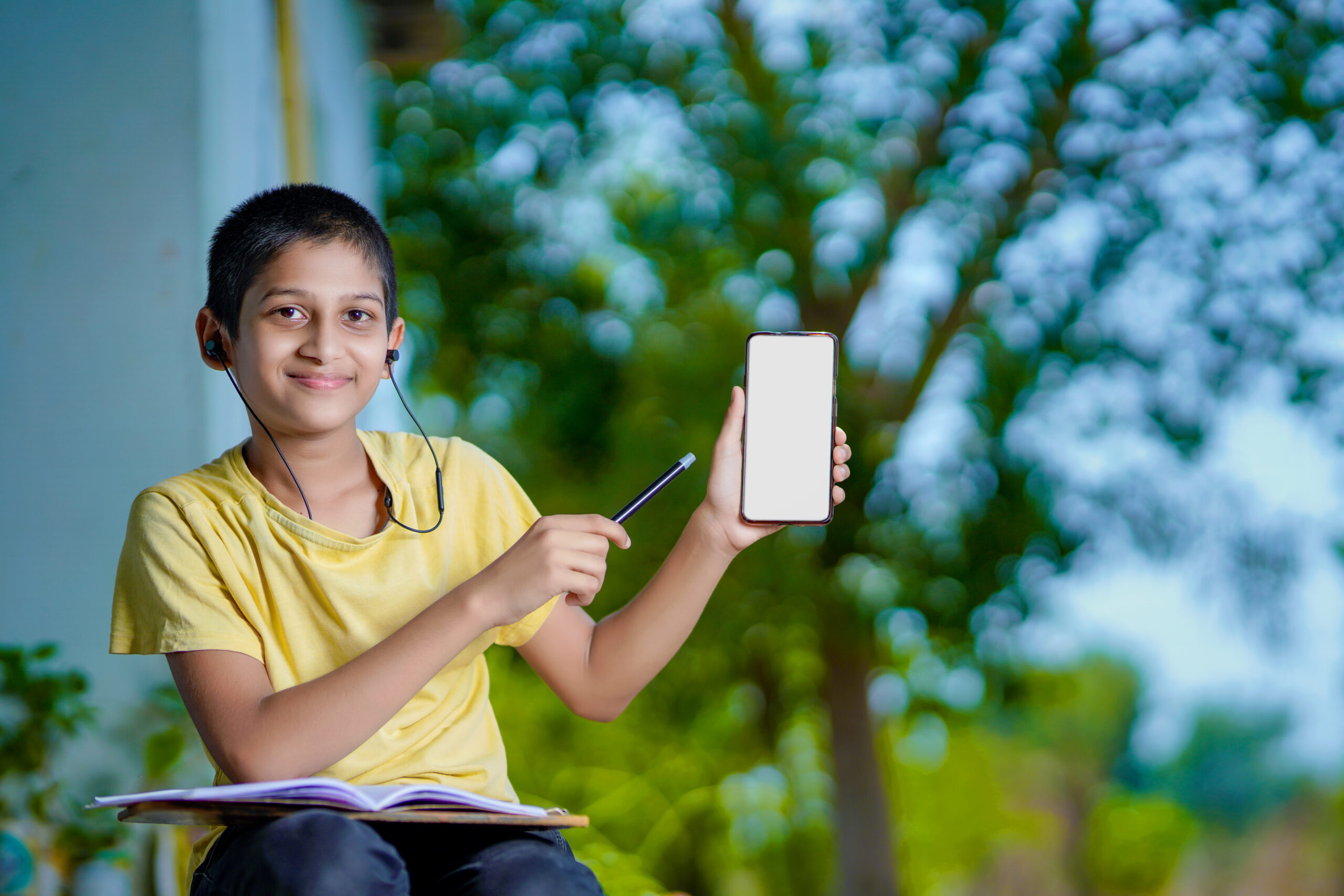Indian school boy holding phone distance learning class using mo Indian school boy holding phone distance learning class using mobile application, watching online lesson, video calling in app making notes studying at home